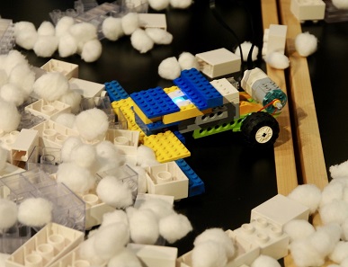 A Lego snowplow plowing cotton balls and Lego pieces.