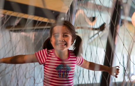 A smiling child holding onto the rope netting of the New Balance Foundation Climb at Boston Children's Museum