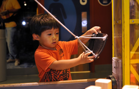 A young child pulling a rope on a yellow-framed rig in the Construction Zone exhibit at Boston Children's Museum