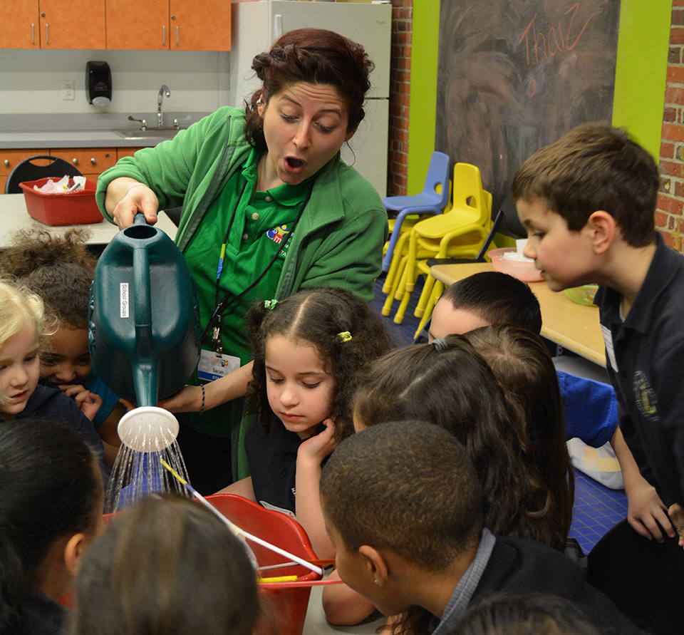 Educator pours water into bucket containing a structure while group of kids observe.