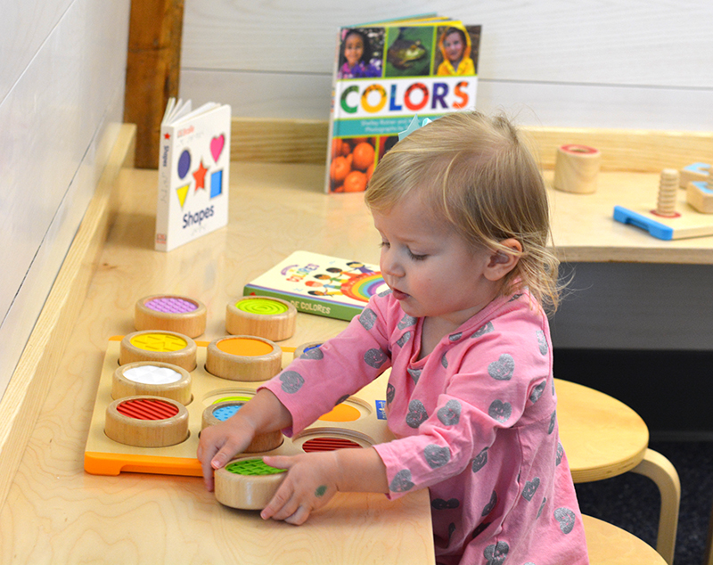 Small child matches colorful wooden pieces to a puzzle with corresponding colors.