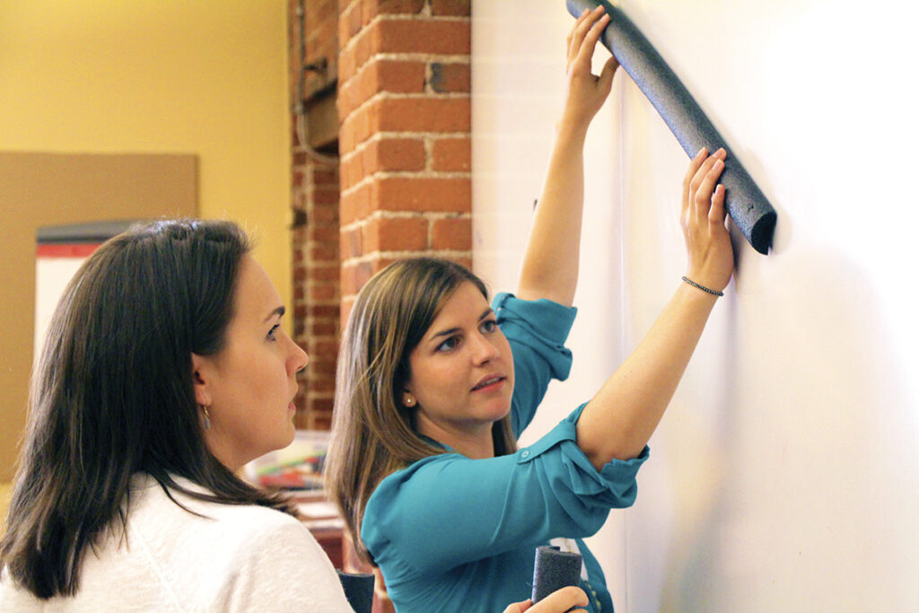 Two educators at a whiteboard holding up a foam tube.