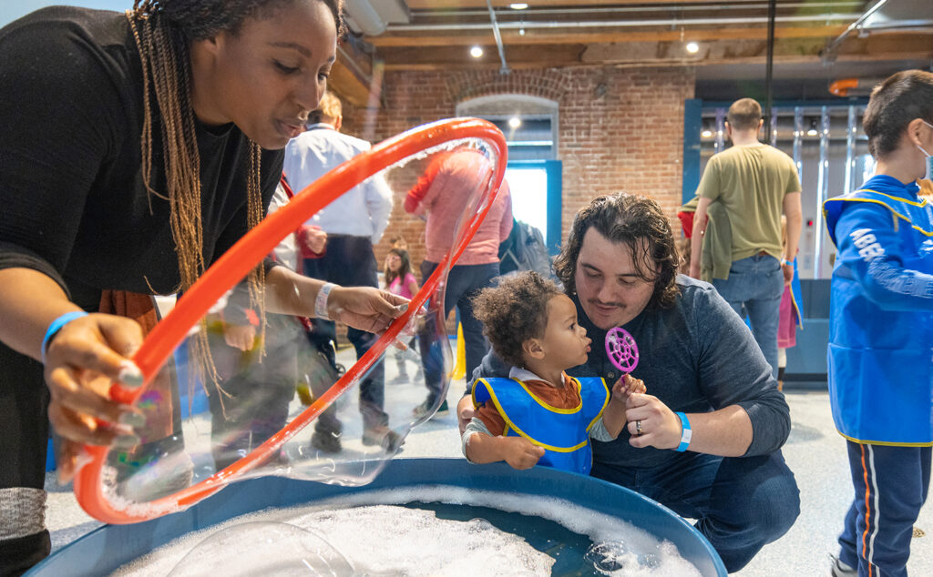 Family blows bubbles together in the Bubbles exhibit.