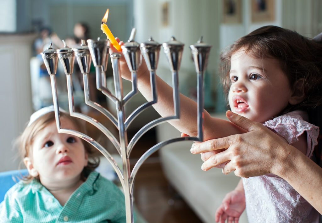 Two kids light a menorah.