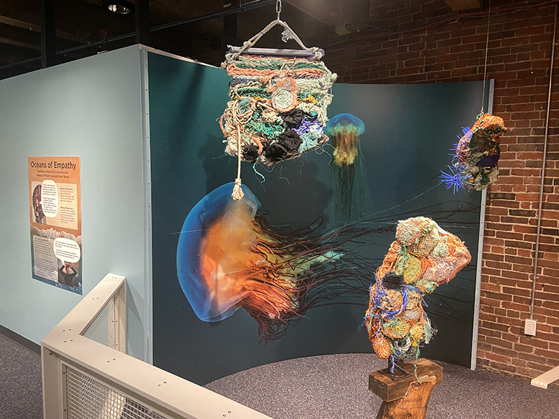 sewn art pieces of thick, colorful yarn hang in front of a mural of jellyfish
